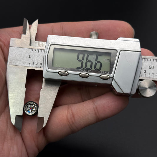 Miniature silver wheel hub set with detailed spokes, shown beside digital caliper
