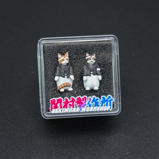 Two cat figurines inside a clear square display case on a dark base