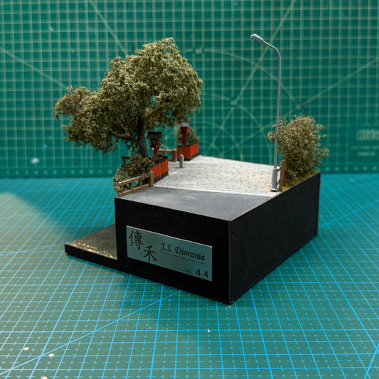 Miniature diorama with black base, trees, stone path, and side logo panel