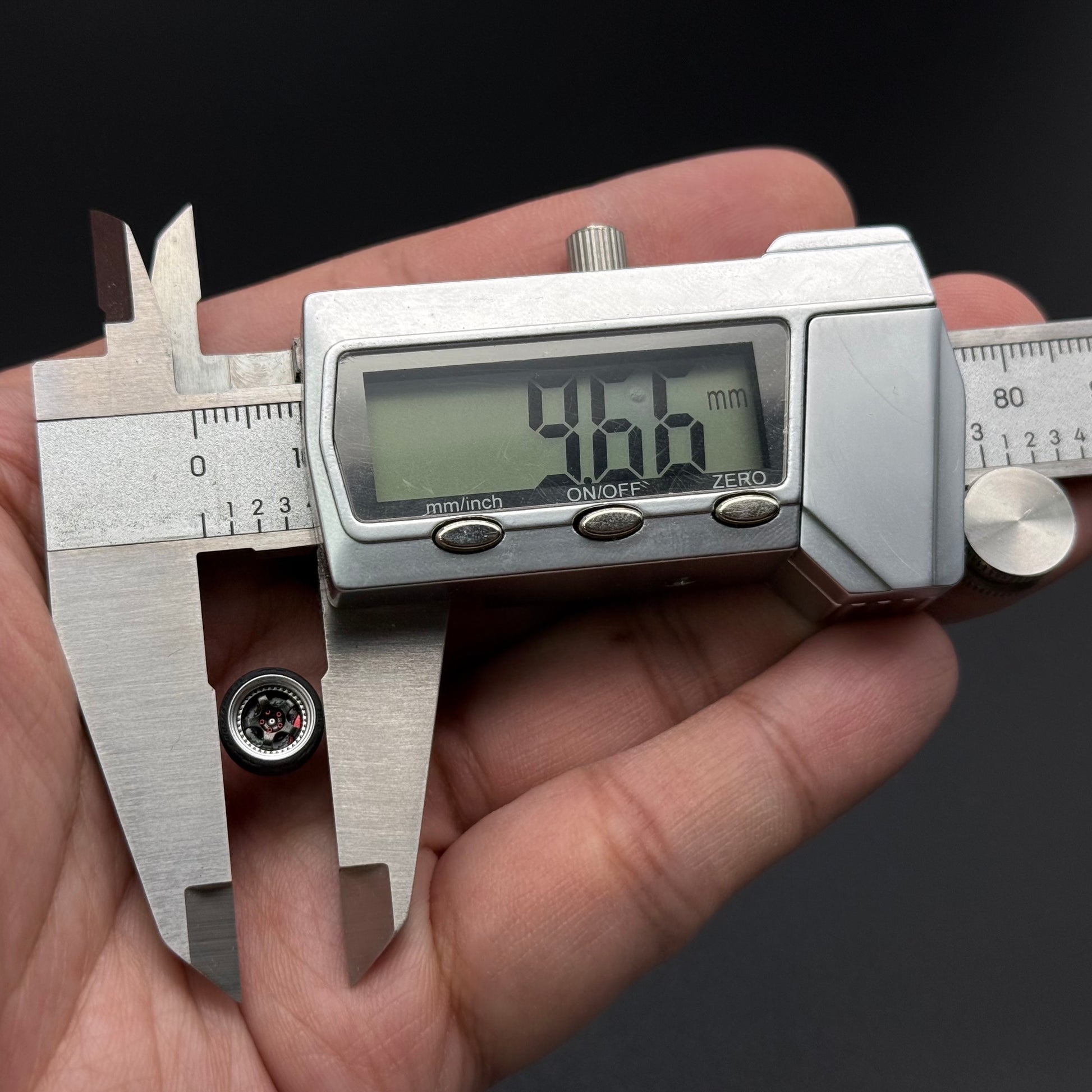 Small gray toy wheel hub with hex lug opening and four circular details, shown with caliper