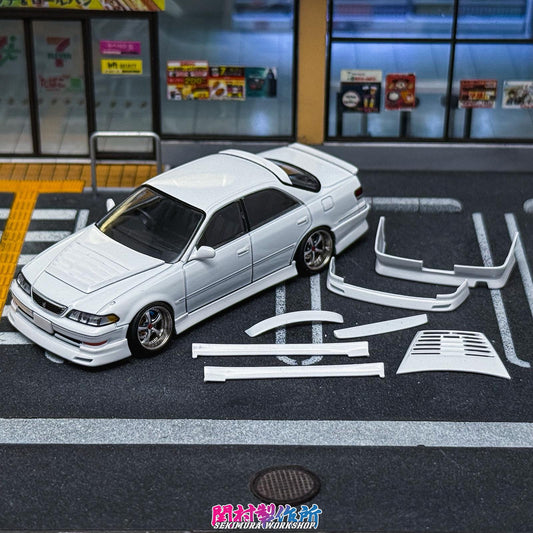 White JZX100 Mark2 model sedan with BN-style body kit parts laid beside it