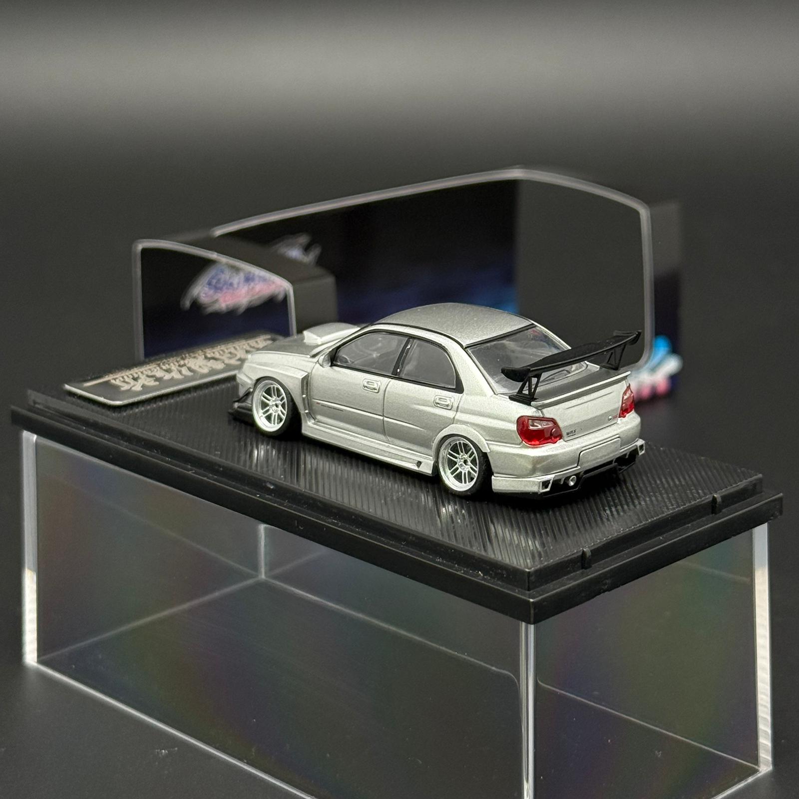 Silver 1/64 sports car model on black display base, rear spoiler and white wheels