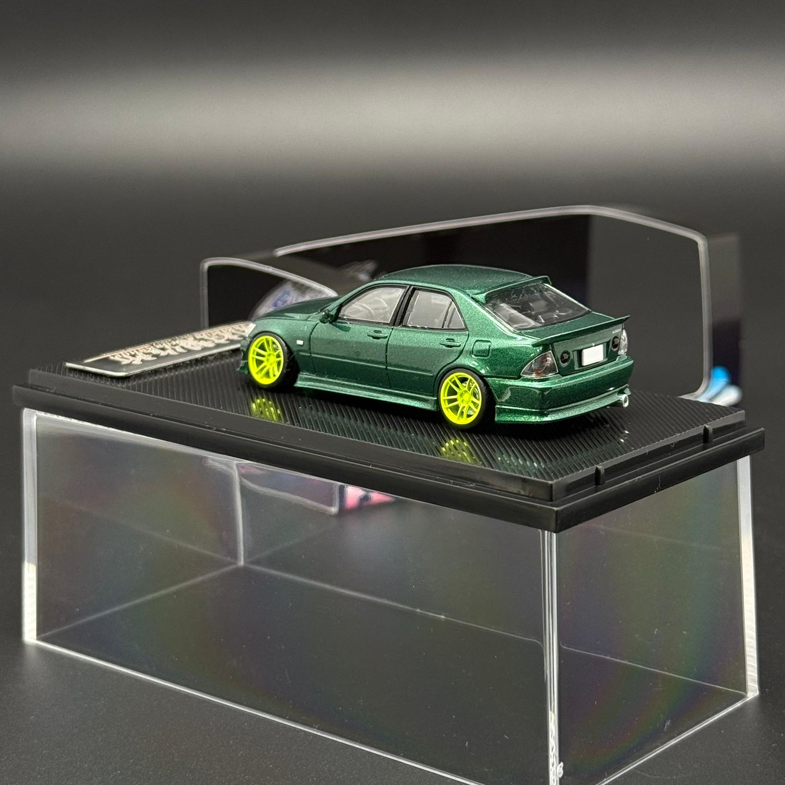 1/64 scale green die-cast car model with yellow wheels on black display base