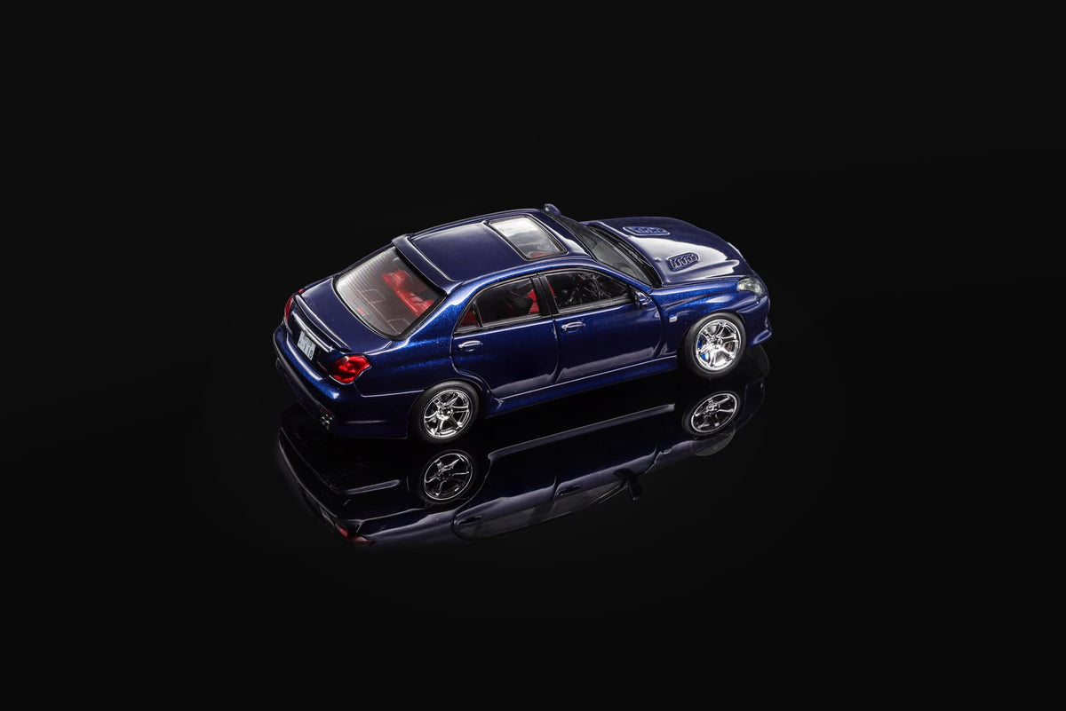 Blue 1/64 scale model sedan, rear-left three-quarter view on reflective base.