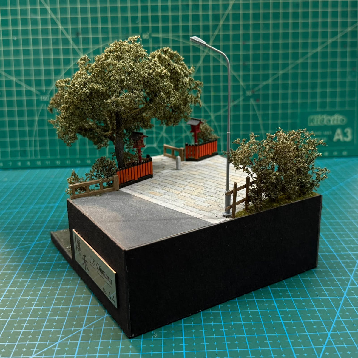 Miniature roadside diorama with stone path, fences, red lantern posts, and lamp