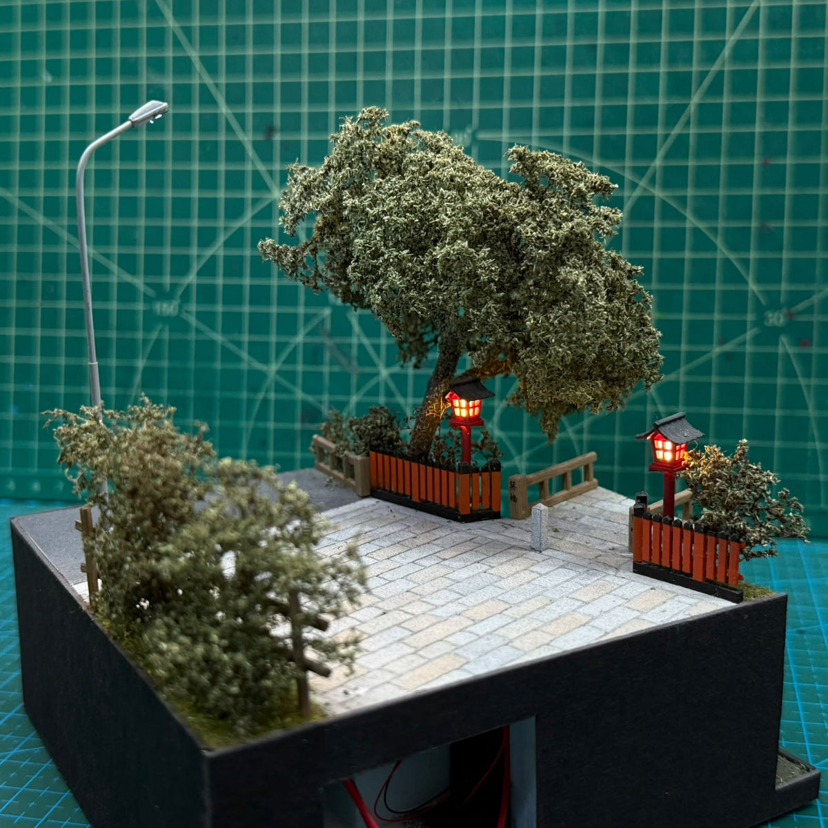 Miniature walkway diorama with roofed red lantern buildings, trees, and a curved lamp