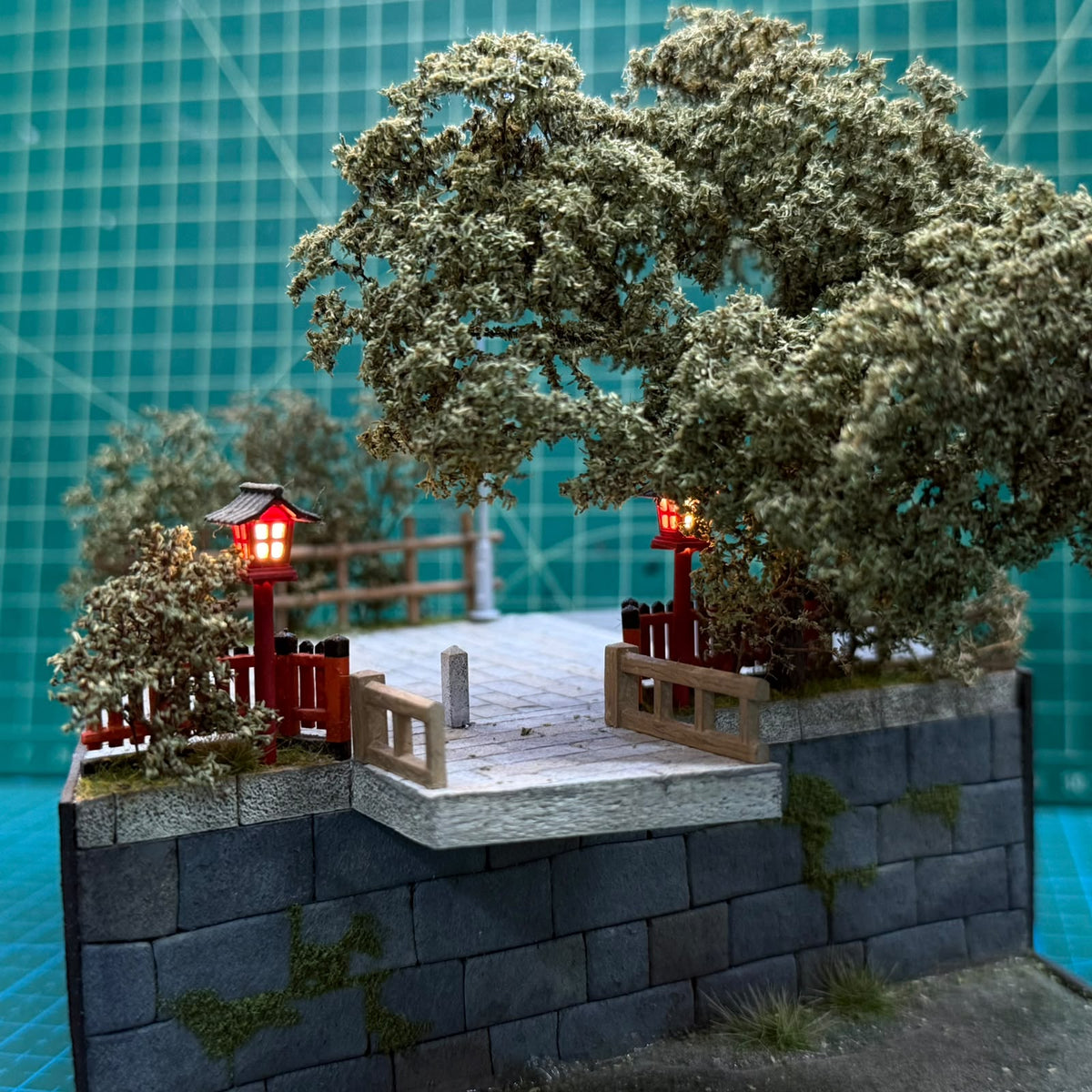 Miniature courtyard diorama with stone platform, two red lantern posts, and trees