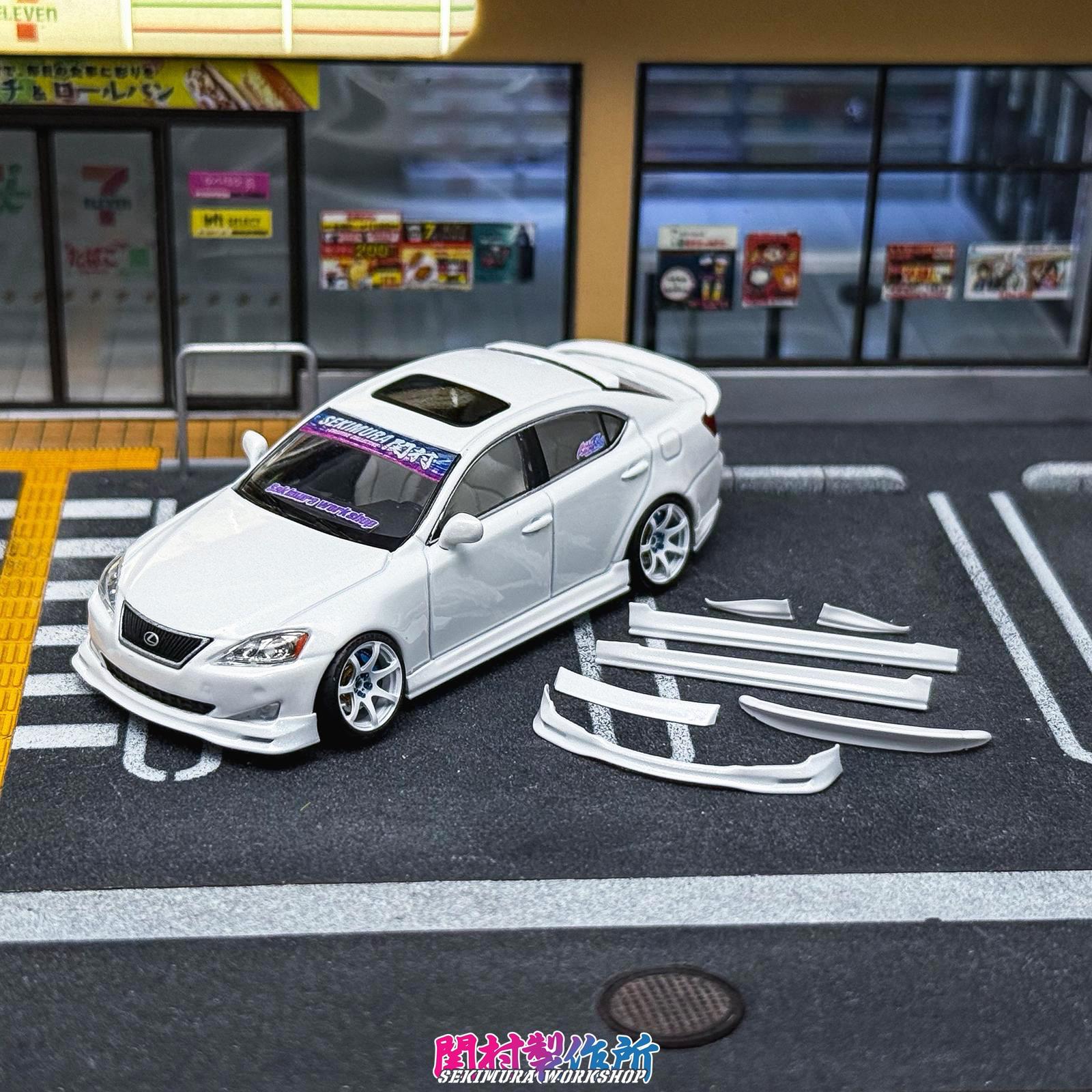 White Lexus IS350-style bodykit car with front splitter and side skirts, parts shown nearby